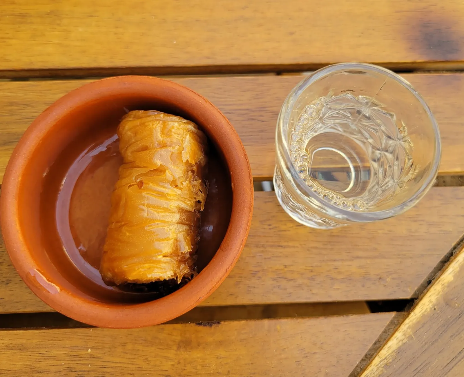 Baklava in a terracotta bowl next to a glass of raki on a wooden table