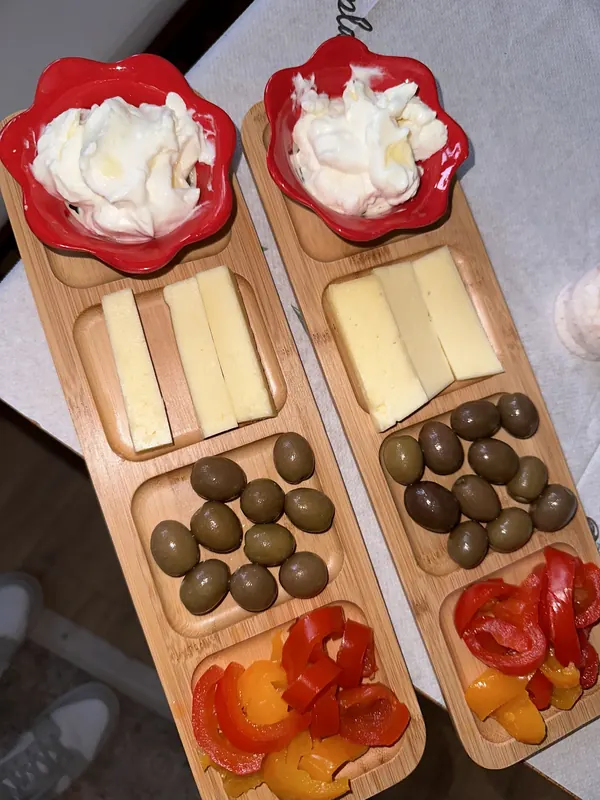 Two wooden boards of yogurt, cheese, olives and roasted peppers