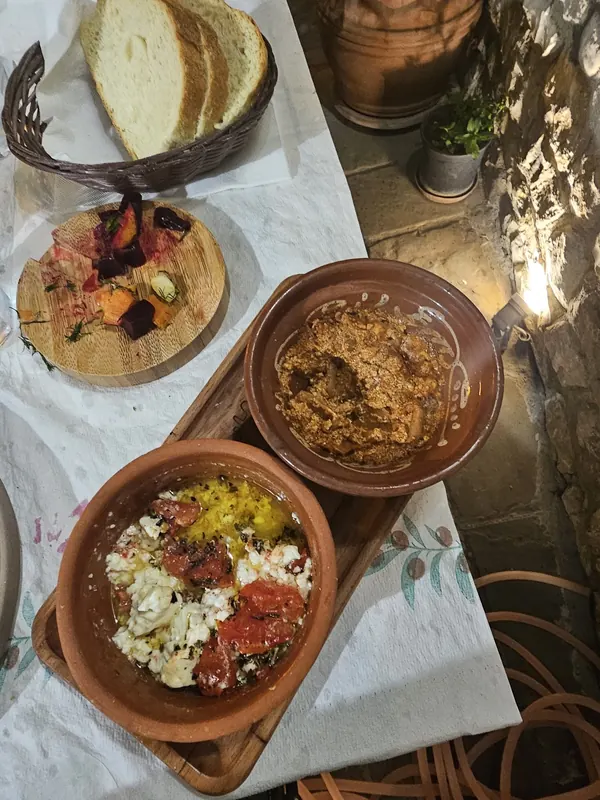 Clay dishes of baked cheese with tomato and a second starter, roasted beetroot on a board and a basket of bread