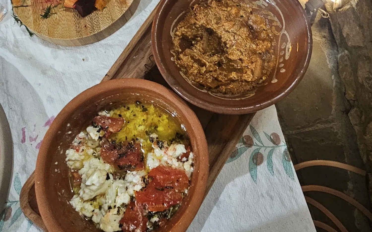 Baked cheese with tomato in a clay dish, beside a second clay bowl and bread