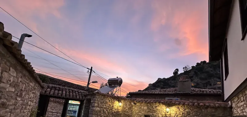The stone courtyard under a pink sunset sky, lanterns lit on the walls and the castle hill behind