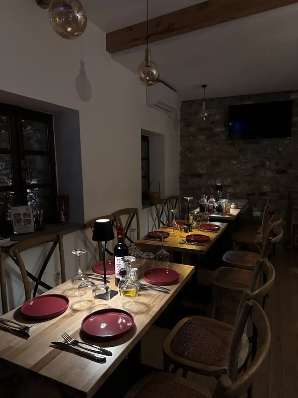 The indoor dining room in black and white: wooden tables set with plates, glasses and a bottle of Amalia wine, a stone wall at the back