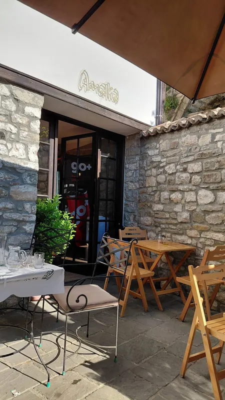 The restaurant entrance under a parasol, a neon Amalia sign above the door and wooden tables in the stone courtyard