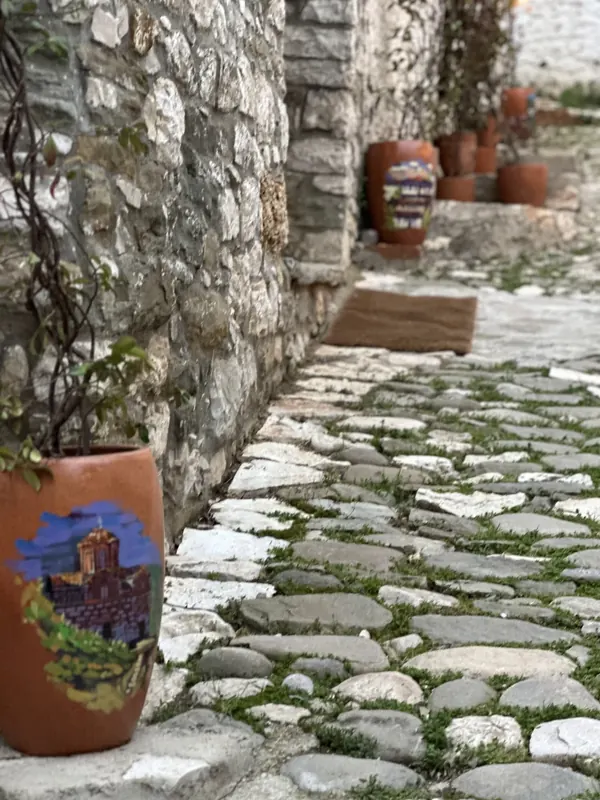 Hand-painted terracotta pots along a stone wall on a mossy cobbled lane