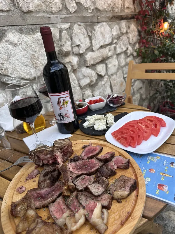 Sliced grilled steak on a wooden board with sliced tomatoes, white cheese, olives and a bottle of red wine