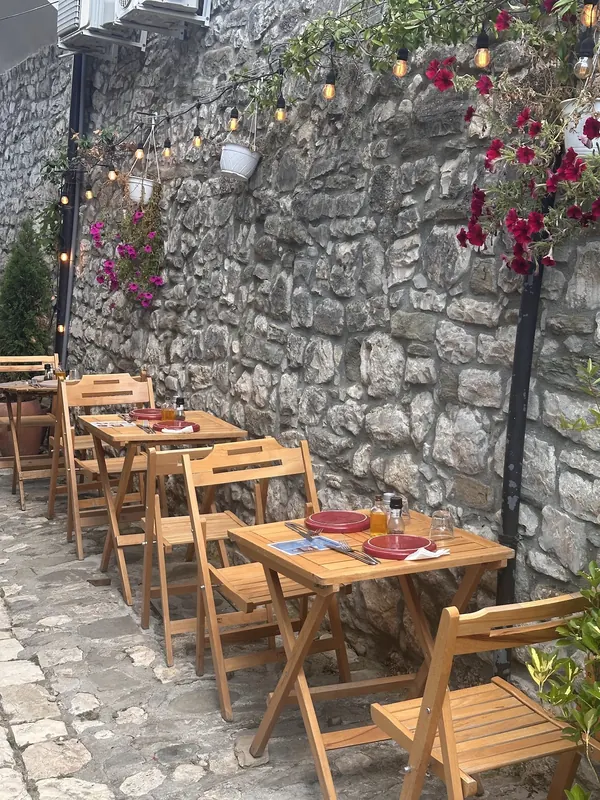 Folding wooden tables along a stone wall hung with petunias and string lights