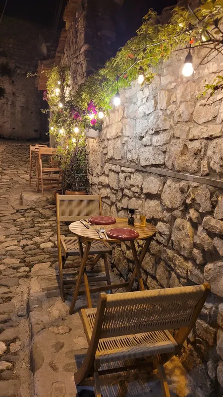 A round table for two set with red plates under string lights and flowers at night
